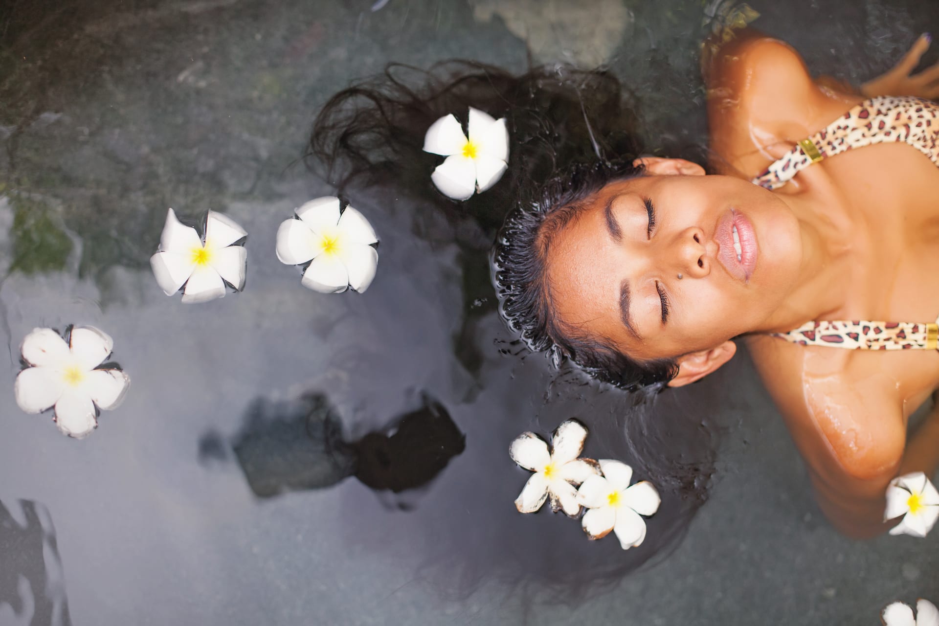 Exotic woman enjoying bath ritual with frangipani flowers